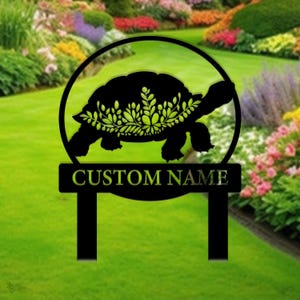 Op de afbeelding: Zwart metalen tuinschild met een silhouet van een schildpad met groene bladeren op zijn rug. Het schild heeft een ronde bovenkant en een rechthoekige onderkant met de tekst "CUSTOM NAME" in geel.