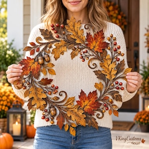 Peut inclure: Une couronne décorative d'automne composée de feuilles de chêne en métal dans des tons orange, jaune et brun, agrémentée de petites baies rouges et de glands bruns. Le design circulaire inclut des branches en métal et le texte VKingCustoms.