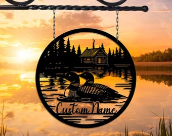 May include: Black metal sign featuring a silhouette of a cabin, trees, and two loons on a lake. The sign is round and has the text "Custom Name" at the bottom.