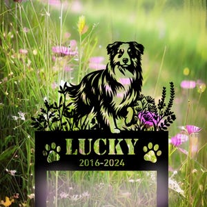 May include: Black metal silhouette of an Australian Shepherd dog with the name "LUCKY" and the dates "2016-2024" on a metal plaque. The silhouette is placed in front of a green grassy background with pink flowers.