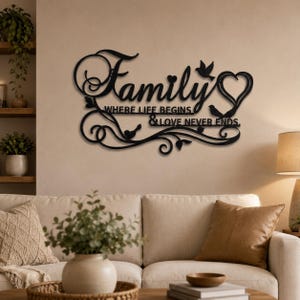 Könnte beinhalten: Ein Wandkunstobjekt aus schwarzem Metall mit dem Wort Family in Schreibschrift, darunter der Text WHERE LIFE BEGINS & LOVE NEVER ENDS. Das Design umfasst dekorative Schnörkel, zwei kleine Vögel und eine herzförmige Kontur.
