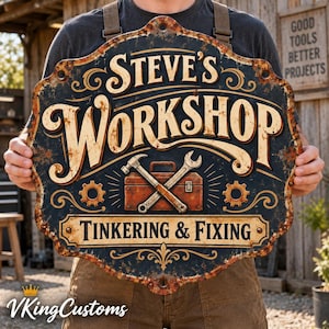May include: A decorative metal sign with a dark blue background and rust-coloured edges. The text reads STEVE'S WORKSHOP and TINKERING & FIXING. A graphic of a toolbox with a crossed hammer and wrench is centred between two gear icons.