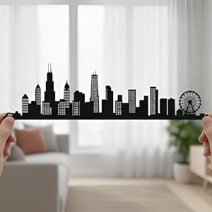 May include: A black silhouette of a city skyline, held between two hands. The skyline features various buildings, including skyscrapers and a Ferris wheel. The design is a decorative piece, possibly for home decor.