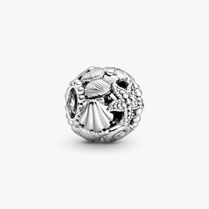 May include: A spherical silver charm bead featuring a detailed relief design of various seashells and a starfish. The surface is textured with intricate carvings of different shell shapes, including a prominent fan-shaped scallop shell. The letters JC appear in the top left corner.