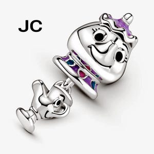 May include: A silver charm depicting a smiling teapot and teacup. The teapot has purple, blue, and pink enamel detailing. The charm has the initials "JC" in black.
