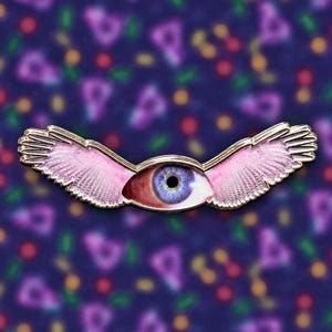 May include: A metal enamel pin featuring a central human eye with a blue iris and a reddish-brown sclera, flanked by two outstretched, detailed pink wings with gold-toned metal edges and defined feather textures throughout the wing design.