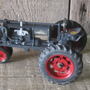 May include: A black toy tractor with red wheels and the word "FARMALL" printed on the side. The tractor has a detailed engine and a seat.
