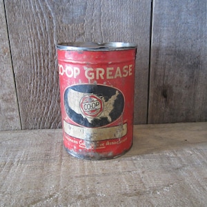 K&ouml;nnte beinhalten: Rote, vintage Metall-Dose mit der Aufschrift "CO-OP GREASE" und einer Karte der Vereinigten Staaten. Die Dose weist Gebrauchsspuren auf. Der Text "CO-OP GREASE" ist wei&szlig;. Die zylindrische Dose steht auf einer Holzoberfl&auml;che. Antikes Design.