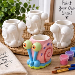 May include: Three unpainted white ceramic snail figurines and one fully painted pink, blue, and green snail figurine. The painted snail has orange eyes. Includes small paint pots, two paintbrushes, and signs reading Paint Your Own Snail and Small Figurine Big Creativity.