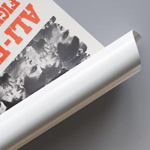 Op de afbeelding: Een opgerolde poster met een zwart-wit afbeelding van gezichten en het woord "ALL" in rode letters.
