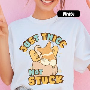 May include: White t-shirt with a cartoon corgi graphic inside a bread bag, and the text "JUST THICC NOT STUCK" in a playful font. The shirt has a crew neck and short sleeves.