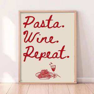 Op de afbeelding: Een ingelijste print met de woorden "Pasta. Wine. Repeat." in rode letters. Daaronder een rode illustratie van spaghetti en een wijnglas. De achtergrond is lichtbeige.