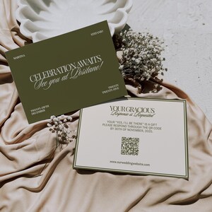 Two olive green and cream wedding stationery cards rest on satin fabric near a decorative white bowl and white flowers.