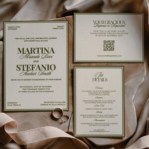 An olive green and cream wedding invitation and details card lie on textured cloth with two silver rings.