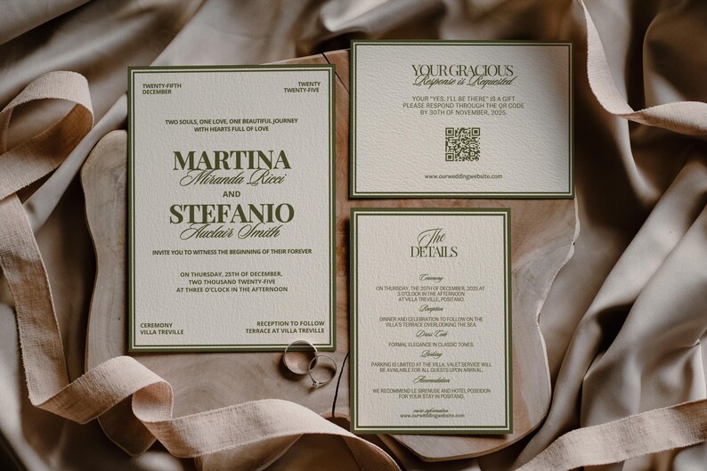 An olive green and cream wedding invitation and details card lie on textured cloth with two silver rings.