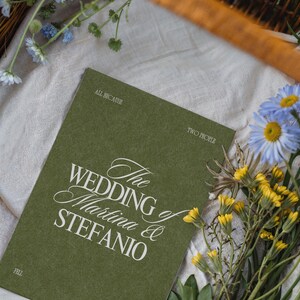 An olive green wedding program card with white text rests in a basket with blue and yellow flowers on cloth.