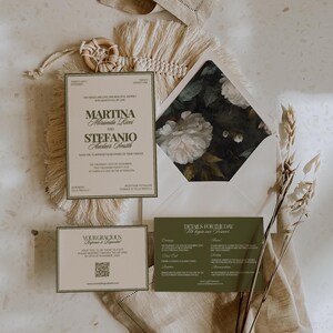 An olive green wedding invitation suite with floral envelope liner lies on a woven mat with dried flowers.
