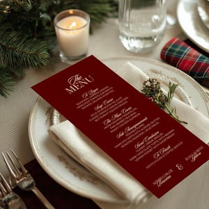 May include: A formal dinner table setting with a burgundy menu card. The menu lists courses like Heirloom Tomato & Burrata and Herb-Crusted Tenderloin. A lit candle, silverware, and a decorative napkin complete the elegant arrangement.