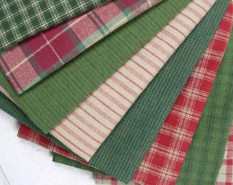 Könnte beinhalten: Eine Sammlung von Stoffmustern mit verschiedenen Designs, darunter grün-weißes Karomuster, rot-grünes Karomuster, einfarbiges Grün und cremefarbene Stoffe mit dünnen roten Streifen. Die Textilien sind fächerförmig angeordnet und zeigen Webmuster.