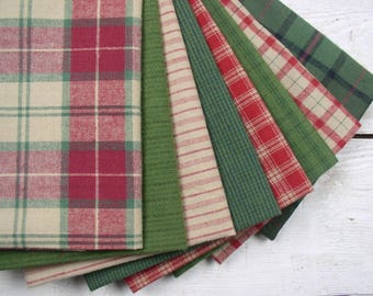 May include: A collection of folded fabric swatches featuring various patterns including red and cream plaid, solid olive green, cream with thin red stripes, dark green grid, and red and green tartan designs arranged in a fan shape.