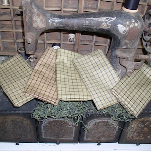 May include: Four fabric squares with a gingham pattern in various colors, including beige, brown, and blue. The squares are arranged on top of a set of three vintage wooden boxes with a rustic finish.