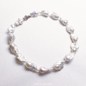 May include: A necklace featuring irregularly shaped, lustrous white pearls strung together with a silver clasp. The pearls have a unique, organic form, reflecting light with a soft sheen. The jewelry is displayed on a white surface.