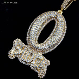 Op de afbeelding: Een goudkleurige hanger met het woord "RICH" in een gestileerd lettertype, ingelegd met talrijke kleine, heldere edelstenen. De hanger heeft een groot, ovaalvormig ontwerp. De woorden "LOST IN ANGELS" staan linksboven.