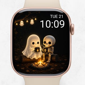 Puede incluir: Un reloj inteligente con correa de color claro y pantalla digital que muestra la hora 10:09 y la fecha TUE 21. La pantalla presenta un gráfico de un fantasma brillante y un esqueleto sentados en un tronco junto a una fogata.