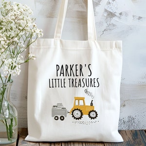 May include: A white canvas tote bag with black text that reads "Parker's Little Treasures". A yellow toy tractor with a gray trailer is printed on the bag.