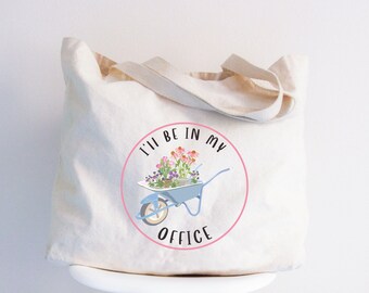 May include: A white canvas tote bag with a pink circle and the text "I'll be in my office" in black. Inside the circle is a blue wheelbarrow with pink and white flowers.