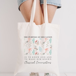 May include: A white tote bag with a floral design and the text "THE PURPOSE OF EDUCATION IS TO KNOW GOD AND TO MAKE HIM KNOWN Classical Conversations".
