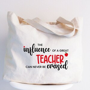 May include: A white canvas tote bag with the text "The influence of a great teacher can never be erased" printed on it. A red apple with a green leaf is included in the text.