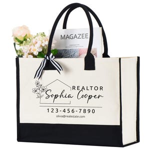 May include: A white canvas tote bag with black trim and handles. The bag has a black and white graphic of a house with flowers and the text "REALTOR Sophia Cooper 123-456-7890 olivia@realestate.com".