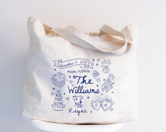 May include: Cream-colored tote bag with blue illustrations and text. The design includes a cake, dog, hearts, and the words "The Williams" and "Reyna". The date "December 14, 2025" and location "Miami, Florida" are also featured.