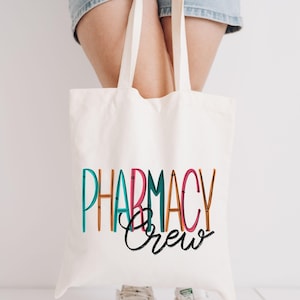 May include: A white canvas tote bag with the text "Pharmacy Crew" in colorful, outlined letters. The text is in a playful, handwritten font.