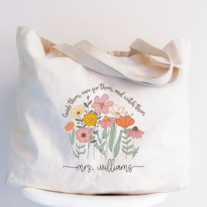 May include: A white canvas tote bag with a floral design and the text "Guide them, care for them, and watch them - mrs. williams".