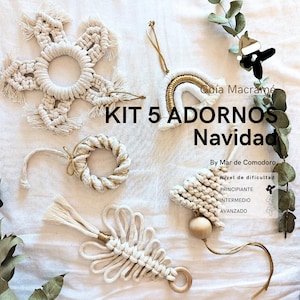 Puede incluir: Un conjunto de cinco adornos navideños de macramé hechos a mano en crema y dorado. Los adornos incluyen un copo de nieve, un arcoíris, una corona, un diseño en forma de corazón y un diseño en forma de árbol. El texto en la imagen dice "KIT 5 ADORNOS Navidad".