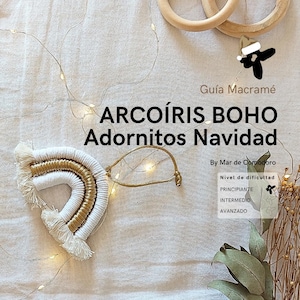 May include: A white and gold macrame rainbow ornament with a tassel fringe. The ornament is hanging from a gold cord. The image includes the text "Arcoíris Boho Adornitos Navidad" and "Guía Macramé".