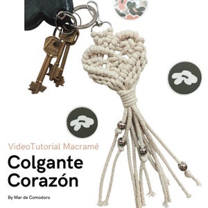 Pode incluir: Um chaveiro de macramé em forma de coração com um tassel e contas prateadas. O chaveiro está preso a um conjunto de chaves.