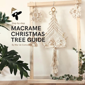 Puede incluir: Una guía paso a paso para hacer un árbol de Navidad de macramé por Mar de Commodore. La imagen muestra un árbol de Navidad de macramé blanco colgado de un marco de madera, con dos copos de nieve de macramé más pequeños a cada lado.
