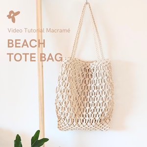 Puede incluir: Un bolso de playa de macramé beige cuelga contra una pared blanca. El bolso tiene un diseño tejido y abierto con dos asas trenzadas. El texto en la imagen dice "Video Tutorial Macramé BEACH TOTE BAG."