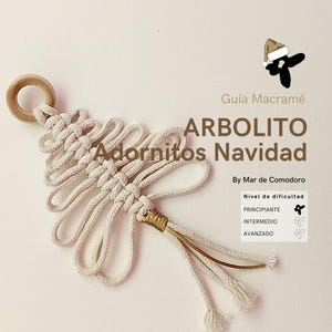 Puede incluir: Un adorno de árbol de Navidad de macramé blanco con un anillo de madera en la parte superior y una borla dorada. El adorno está etiquetado como "Arbolito Adornitos Navidad" y "Guia Macrame".