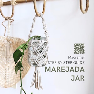 以下が含まれることがあります： 白いマクラメ製のプラントハンガーに、ガラスの瓶と緑色の植物が入っています。ハンガーは竹製の棚に掛けられています。ハンガーの下には「Macrame STEP BY STEP GUIDE MAREJADA JAR」というテキストが書かれています。