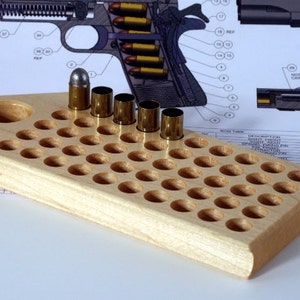 May include: A light-colored wooden ammunition loading block with multiple circular holes. Several brass cartridge casings and one silver-tipped bullet are placed in the block. A diagram of a firearm is in the background.