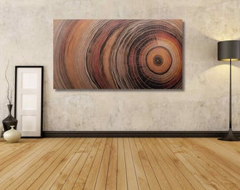 May include: A rectangular wall art piece featuring a detailed, high-contrast print of concentric tree ring patterns in shades of deep brown, burnt orange, and black, displayed horizontally on a textured wall above a wooden floor.