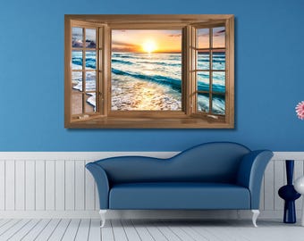 May include: A rectangular wall decal featuring a realistic wooden window frame with open shutters, displaying a scenic ocean view at sunset with golden light reflecting on blue waves and a sandy beach, mounted on a solid blue wall above a blue sofa.