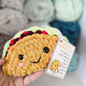 May include: A crocheted taco plush toy with a smiling face and a tag that reads "Emotional Support Taco. It's okay to fall apart sometimes. Tacos fall apart and we still love them."