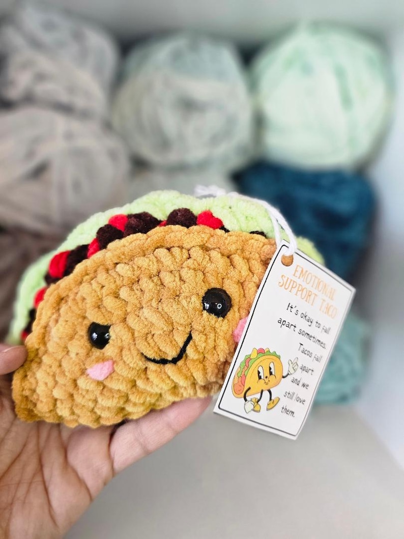 May include: A crocheted taco plush toy with a smiling face and a tag that reads "Emotional Support Taco. It's okay to fall apart sometimes. Tacos fall apart and we still love them."
