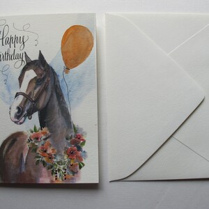 May include: A watercolor painting of a brown horse with a white blaze on its face. The horse is wearing a brown halter and has a floral garland around its neck. A brown balloon is floating above the horse. The card says "Happy Birthday".