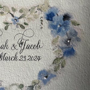 Puede incluir: Una invitaci&oacute;n de boda con un dise&ntilde;o floral de acuarela en tonos azules y verdes. La invitaci&oacute;n dice "Sarah & Jacob" y "March 23, 2024".